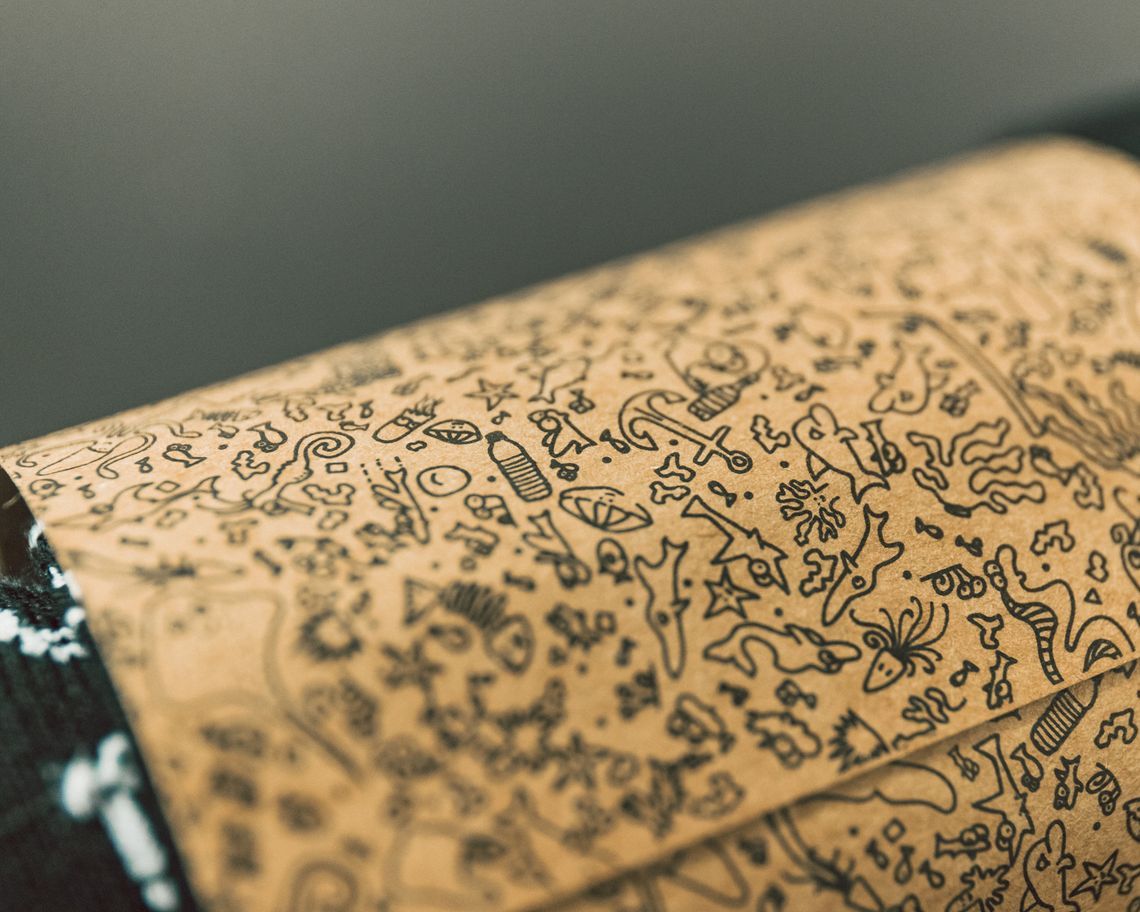 Close-up of patterned paper wrapping with sketched icons, highlighting parcels shipped plastic-free, sustainability storytelling, and a small-brand fulfilment aesthetic with circular organic cotton clothing relevance