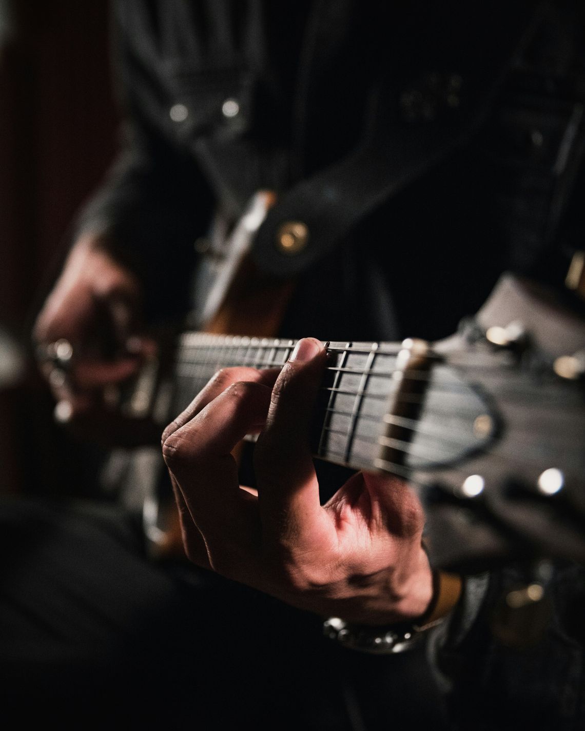 Guitarist’s hand close-up fretting strings in a dark studio setting, grounding real-player identity, sustainable organic cotton musician merch culture, and overall streetwear relevance for hoodie and tee shoppers. sustainable fashion Above Average Clothing